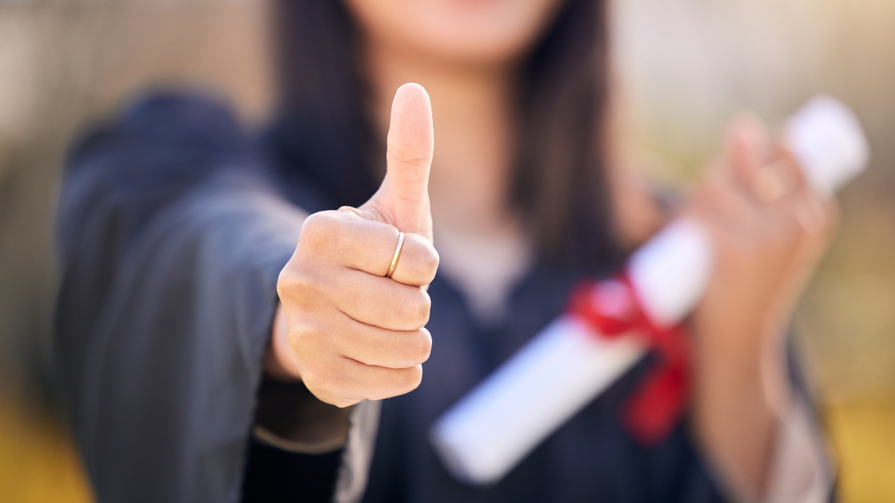 Studentkinja pokazuje palac gore nakon uspešno dobijene stipendije ili kredita